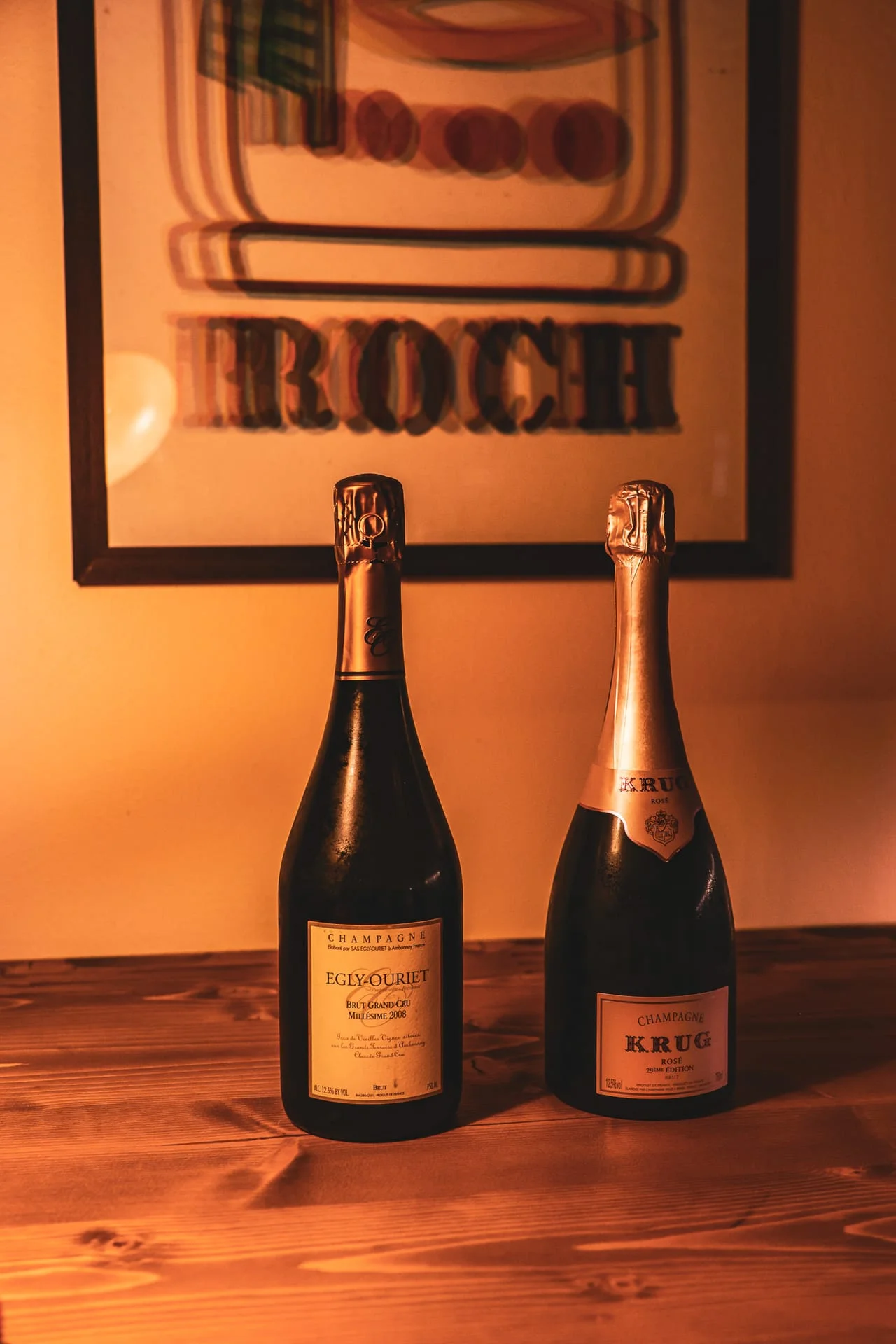 Due bottiglie di champagne sul tavolo in legno, davanti a un poster d'epoca